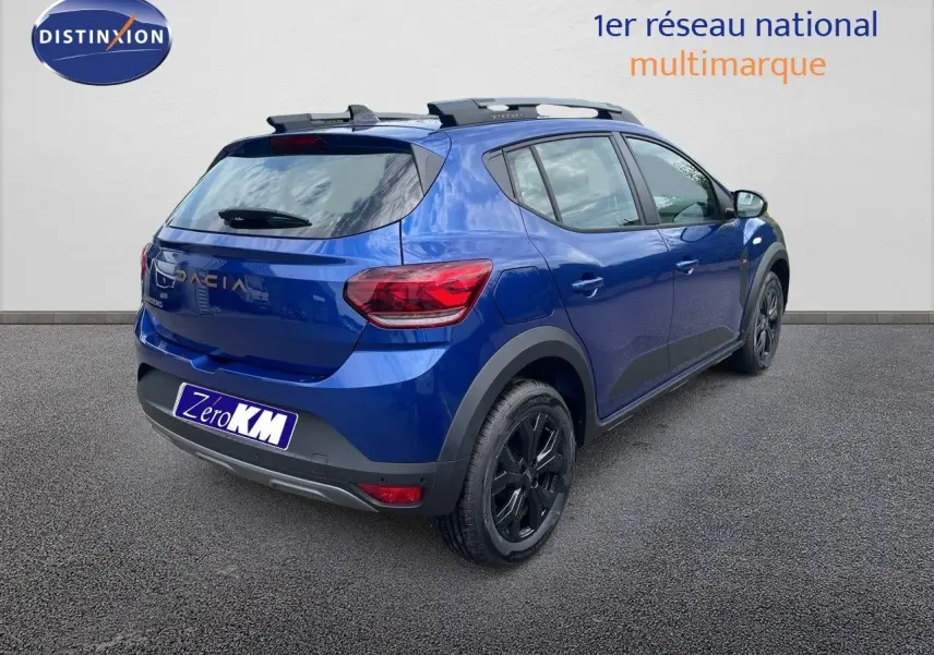 Vue 3/4 arrière droite d'une Dacia Sandero Stepway 2024 bleu iron metal avec jantes noires et barres de toit.