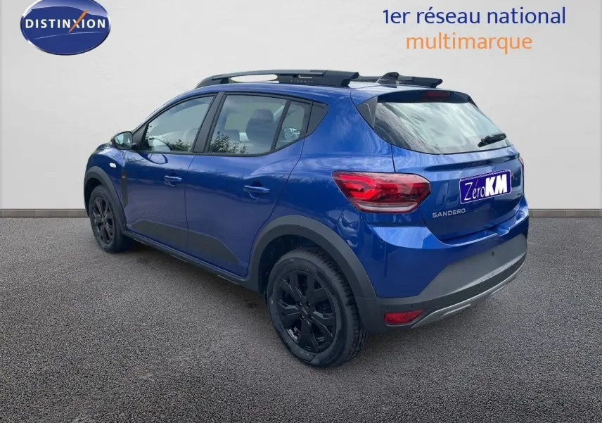 Vue 3/4 arrière côté gauche d'une Dacia Sandero Stepway 2024 bleu Iron Metal avec jantes noires et barres de toit.