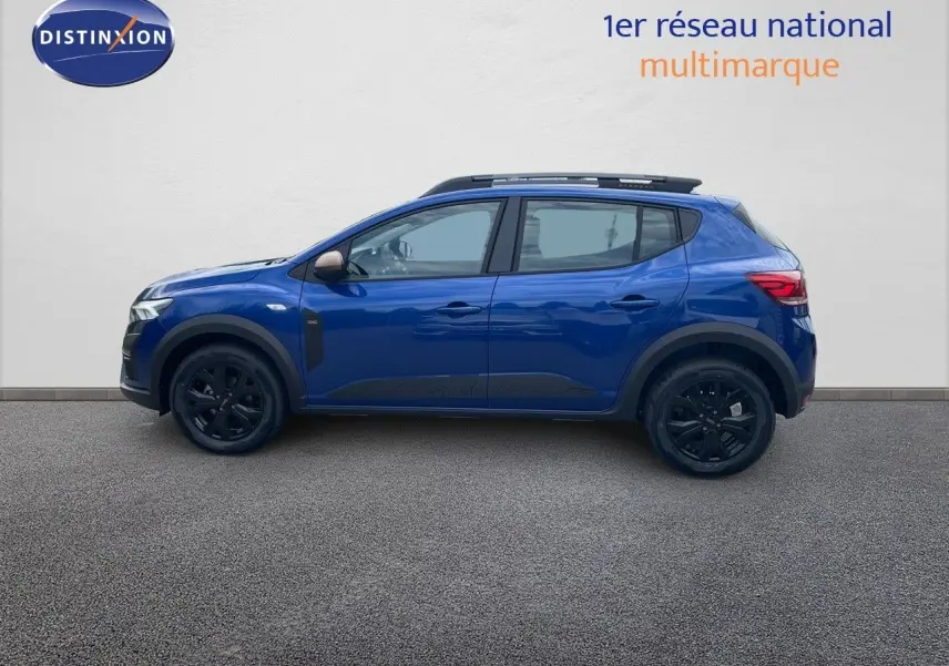 Profil côté gauche d'une Dacia Sandero Stepway 2024 bleu iron metal avec jantes noires et barres de toit.