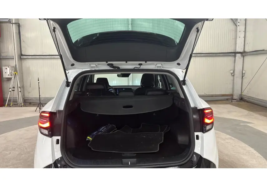 Coffre ouvert d'un KIA Sportage blanc 2022 vu de l'arrière avec tapis de sol et hayon relevé en intérieur d'entrepôt.
