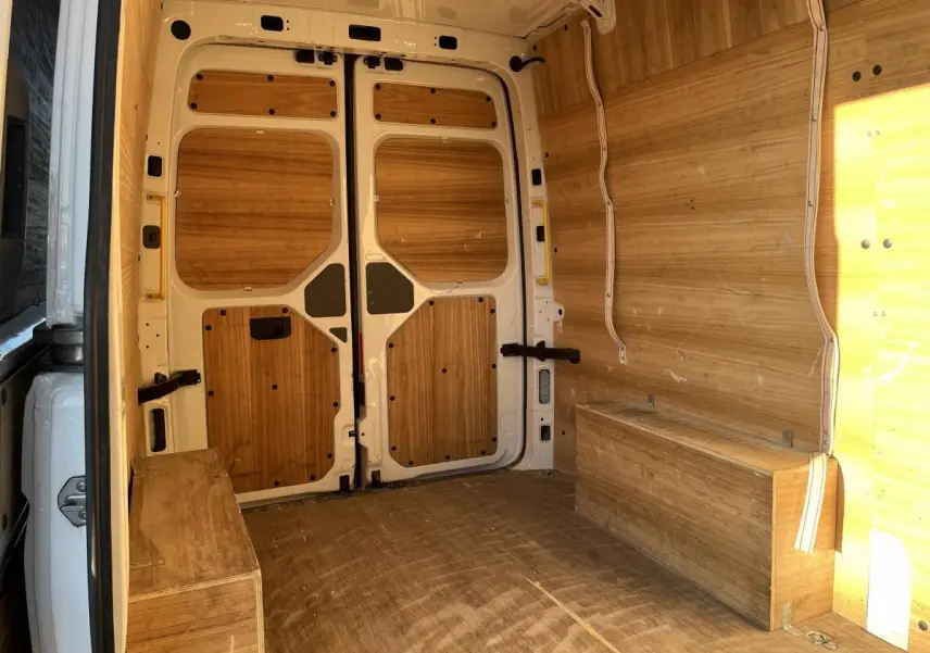 Intérieur du fourgon Volkswagen Crafter blanc vu de l'arrière, avec aménagements en bois sur les parois et le plancher.