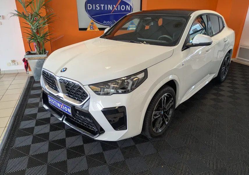 BMW X2 sDrive blanc alpin vue de profil côté gauche, avec jantes sport et toit panoramique en intérieur showroom.