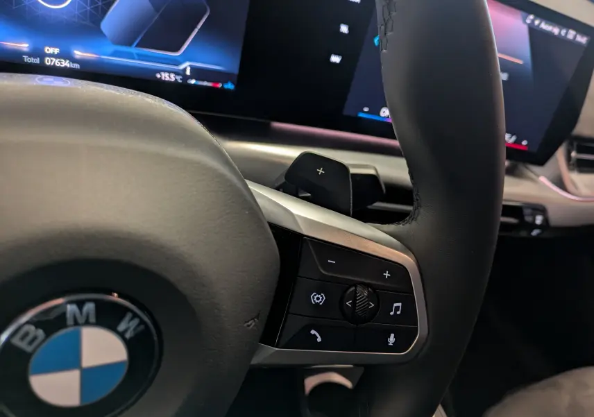 Détail du volant noir et tableau de bord numérique du BMW X2 sDrive blanc avec commandes multifonctions et éclairage d'ambiance rose.