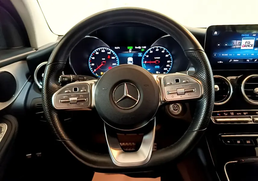 Vue rapprochée du volant cuir et alu d'une Mercedes GLC 300 E AMG Line 2021 avec tableau de bord numérique allumé.