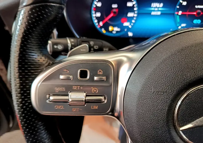 Gros plan sur les commandes à gauche du volant cuir noir du Mercedes GLC 300 E AMG Line 2021 avec tableau de bord numérique bleu.