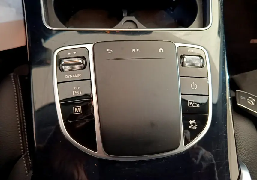 Gros plan sur la console centrale noire brillante du Mercedes GLC 300 E AMG Line avec commandes tactiles et molette volume.