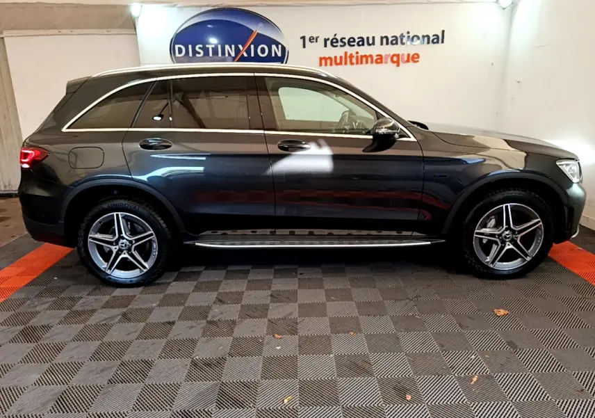 Profil côté droit d'un Mercedes GLC 300 E AMG Line gris foncé avec jantes alliage et vitres teintées en intérieur showroom.