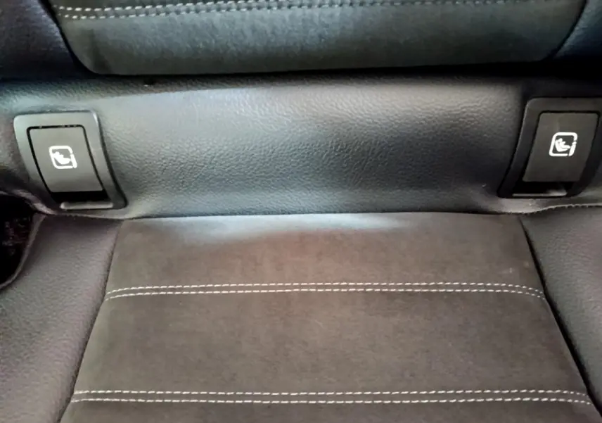 Gros plan sur la commande de rabattement des sièges arrière en cuir noir avec surpiqûres blanches dans un Mercedes GLC gris foncé.