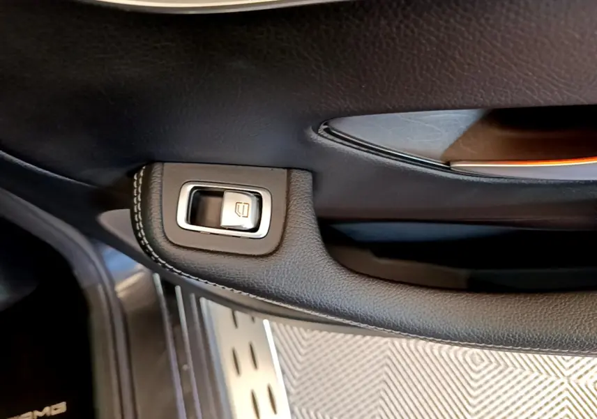 Gros plan sur la poignée intérieure noire avec bouton de lève-vitre du Mercedes GLC 300 E AMG Line gris foncé.