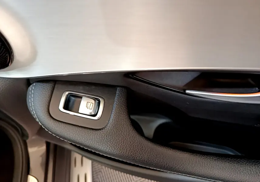 Gros plan sur la commande de lève-vitre en cuir noir et aluminium sur la portière côté conducteur du Mercedes GLC gris foncé.