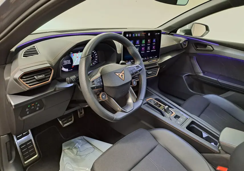 Vue intérieure côté conducteur de la CUPRA LEON ST 2025 avec tableau de bord numérique et éclairage d’ambiance violet.