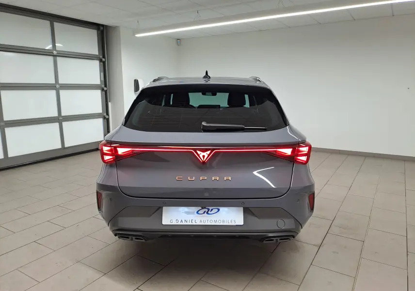 Vue arrière d'une CUPRA LEON ST 2.0 TDI 150 DSG7 en gris Graphène avec feux arrière allumés dans un garage.