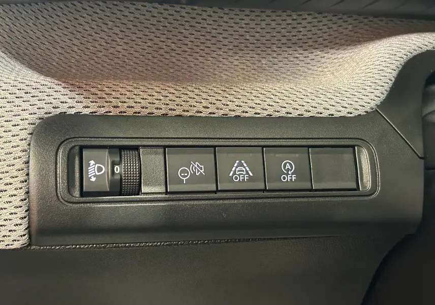 Gros plan sur les commandes de réglage des phares et aides à la conduite dans une Citroën C3 gris Artense, intérieur tissu gris.