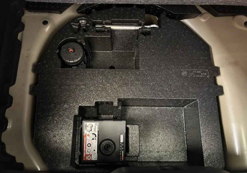 Vue rapprochée du compartiment de rangement sous le coffre d'une Citroën C3 gris Artense, montrant le compresseur de pneu intégré.