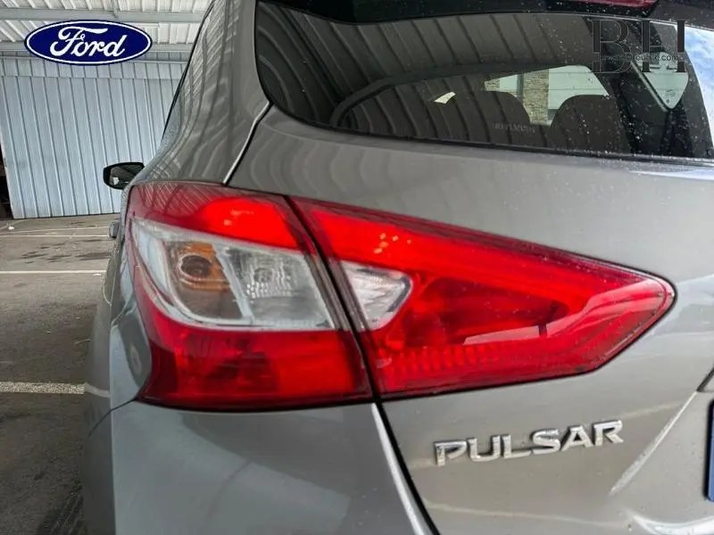 Gros plan sur le feu arrière droit d'une Nissan Pulsar gris clair avec logo et hayon visible.