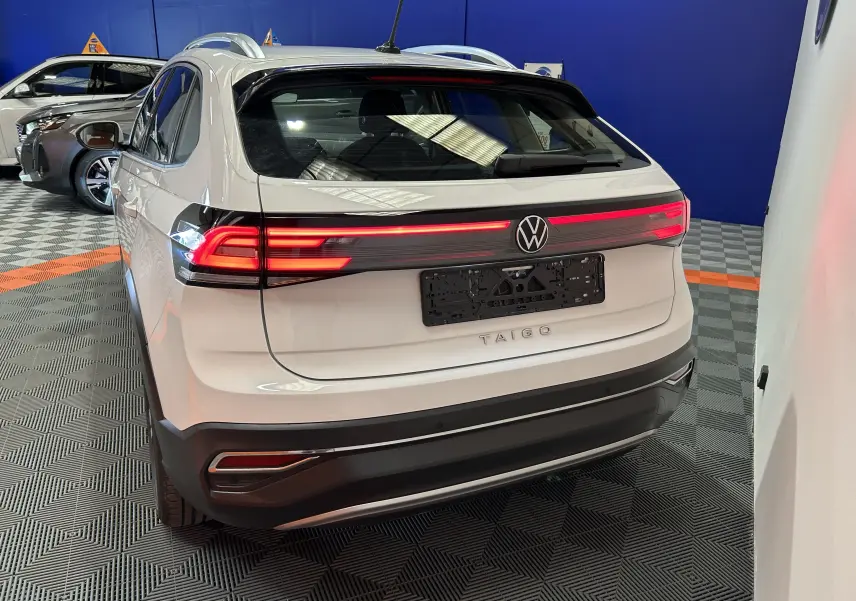 Vue 3/4 arrière droite du Volkswagen Taigo blanc pur avec feux arrière LED allumés dans un showroom.