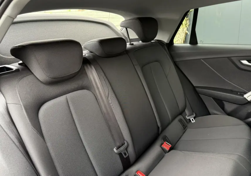 Vue intérieure montrant la banquette arrière noire du SUV Audi Q2 35 TFSI S-Line, avec appuie-têtes et ceintures visibles.