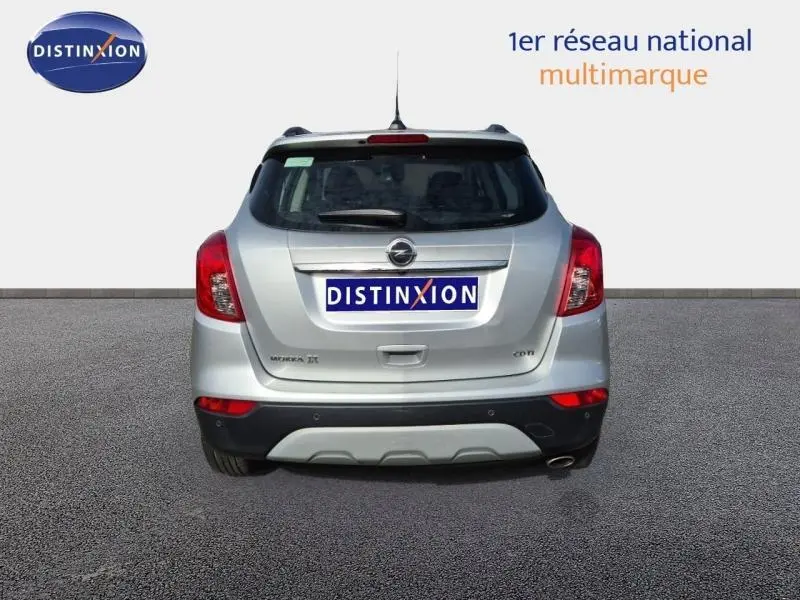 Vue arrière d'un Opel Mokka X gris minéral avec feux rouges et pare-chocs noir contrastant, sur fond neutre.