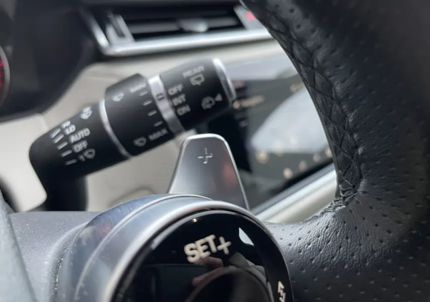 Gros plan sur la commande SET+ au volant en cuir noir du Range Rover Velar Silicon Silver, intérieur beige visible en arrière-plan.