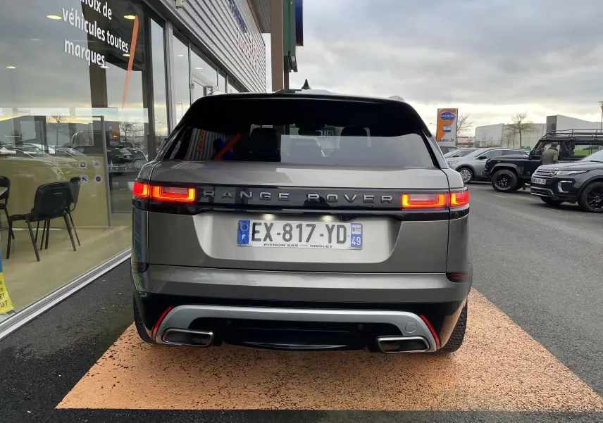Vue arrière d'un Range Rover Velar D300 gris silicon silver avec feux allumés, garé devant un showroom.