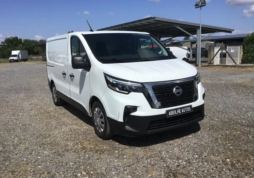 Fourgon blanc Nissan Primastar L1H1 vu en 3/4 avant droit sur un parking extérieur ensoleillé.
