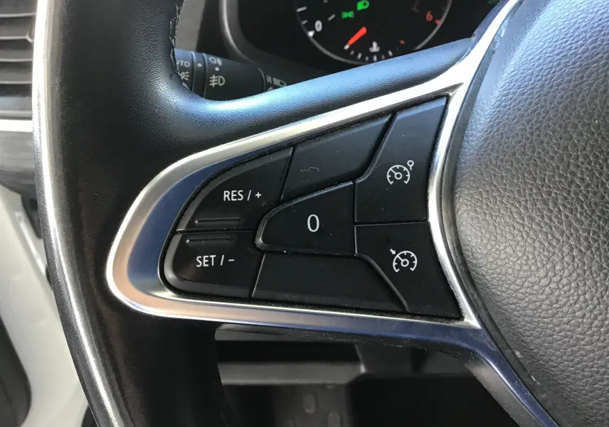 Gros plan sur les commandes de régulateur de vitesse au volant d'un Nissan Primastar blanc, tableau de bord en arrière-plan.