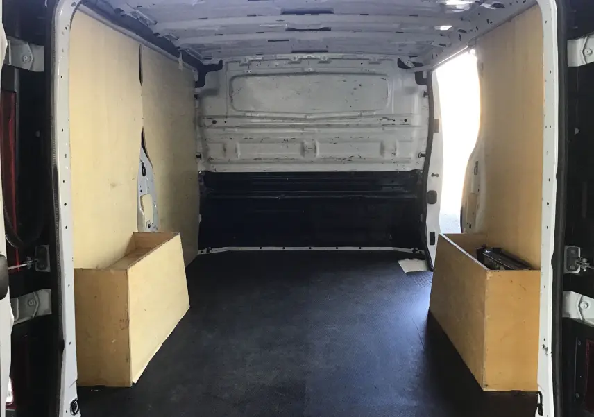 Vue intérieure arrière du fourgon blanc Nissan Primastar L1H1 2022 avec aménagements en bois sur les côtés du compartiment de chargement.