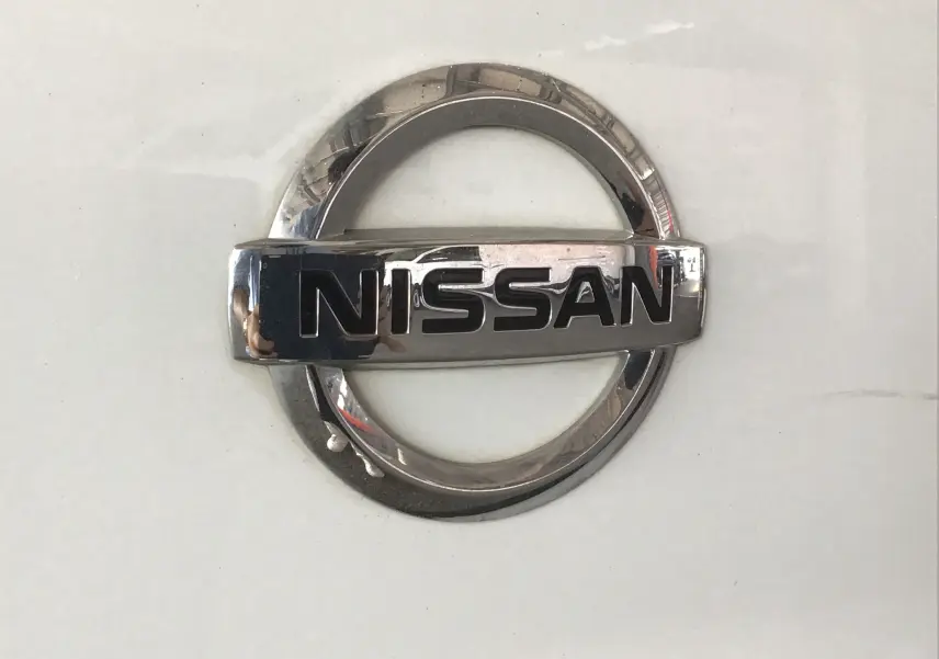 Gros plan sur l'emblème chromé Nissan sur fond blanc du fourgon Primastar L1H1 2022.