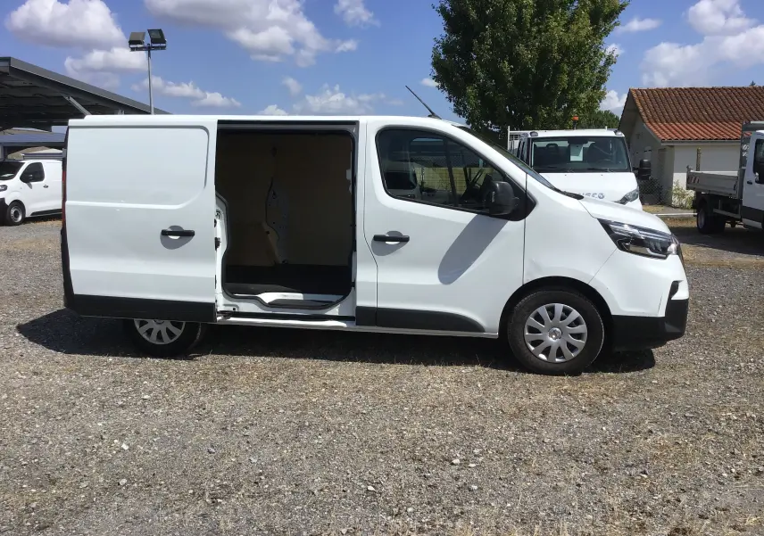 Nissan Primastar blanc vu de profil côté droit avec porte latérale coulissante ouverte sur parking extérieur.