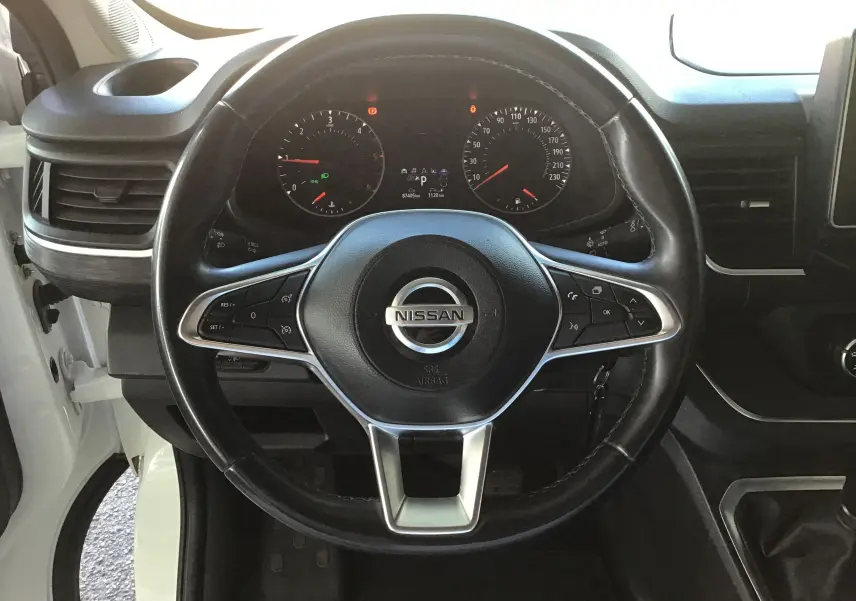 Vue intérieure centrée sur le volant noir du Nissan Primastar Fourgon blanc, avec tableau de bord et commandes visibles.