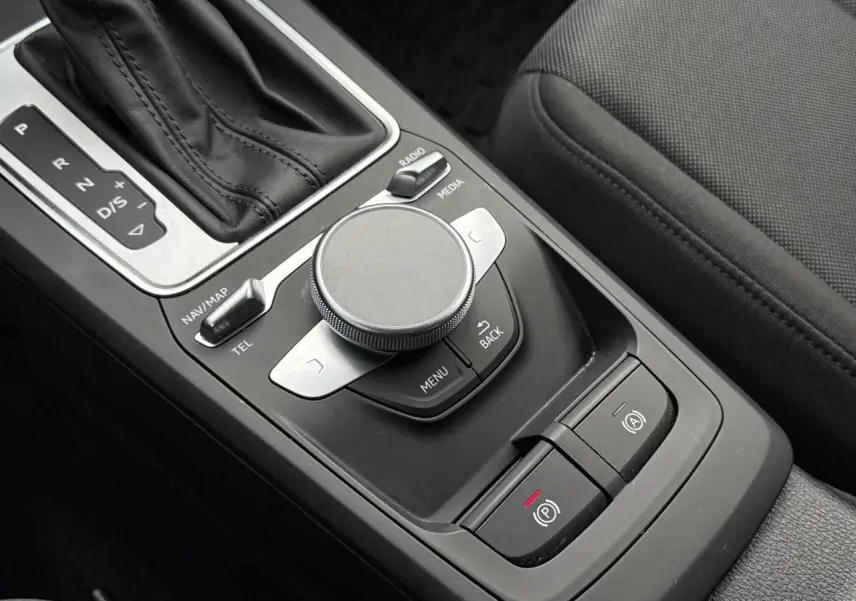 Gros plan sur la console centrale noire de l'Audi Q2 35 TFSI S-Line avec molette de commande et levier de boîte automatique.