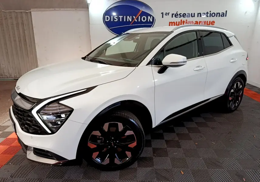KIA SPORTAGE blanc en 3/4 avant droit, mettant en valeur ses phares LED en forme de flèche et ses jantes noires distinctives.