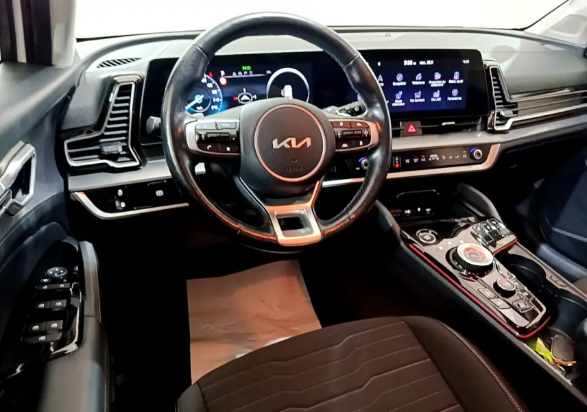 Vue intérieure avant du KIA SPORTAGE 2022 avec volant cuir, tableau de bord numérique et console centrale high-tech noire.