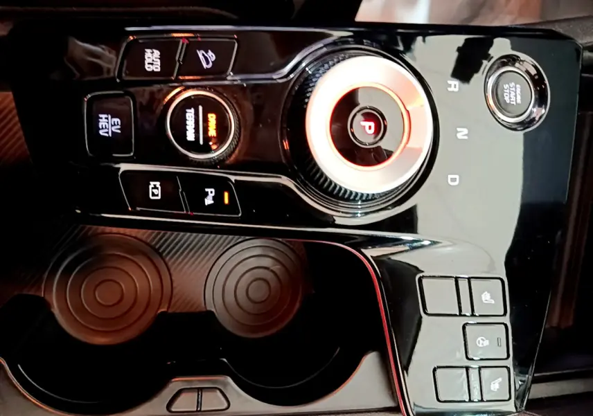 Gros plan sur la console centrale noire brillante du Kia Sportage hybride rechargeable 2022 avec molette de sélection et boutons lumineux.