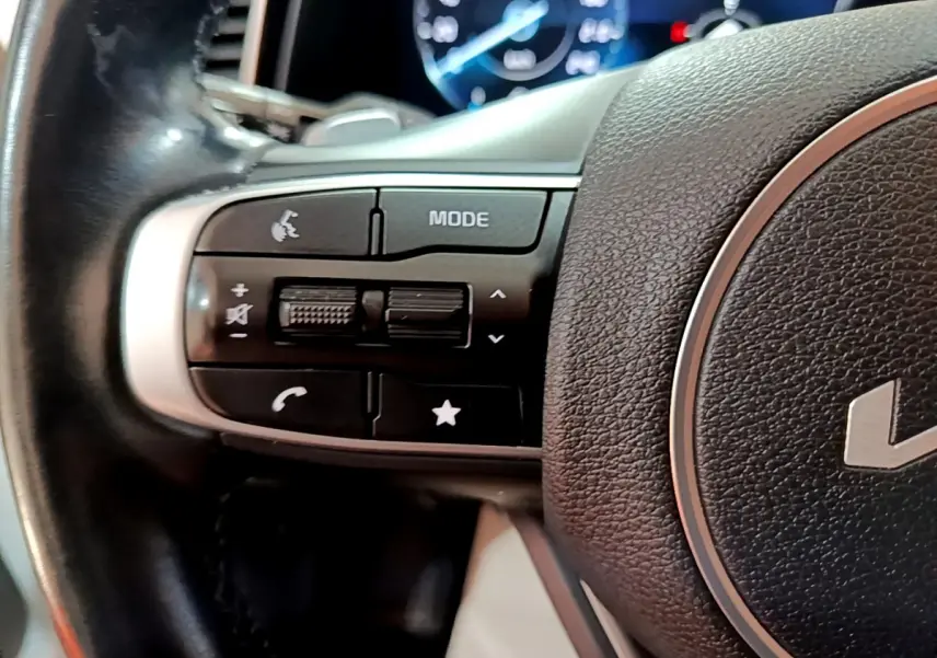 Gros plan sur les commandes gauche du volant cuir noir du Kia Sportage blanc 2022 avec affichage digital en arrière-plan.