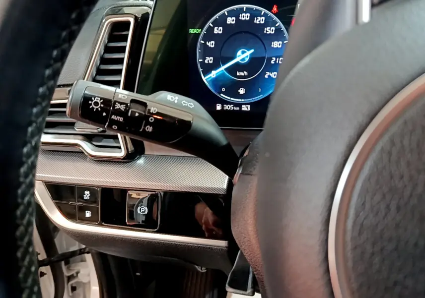 Gros plan sur le tableau de bord et volant du Kia Sportage hybride blanc, affichage numérique et commandes lumineuses visibles.