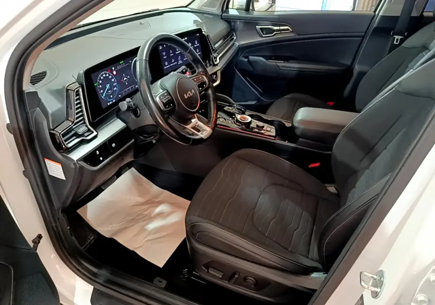 Intérieur avant droit du KIA SPORTAGE blanc 2022, avec tableau de bord numérique et sièges noirs en tissu.