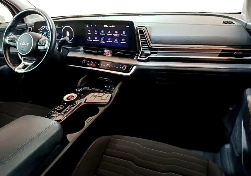 Vue intérieure du tableau de bord et console centrale du Kia Sportage hybride rechargeable 2022, avec écran tactile large et volant cuir noir.