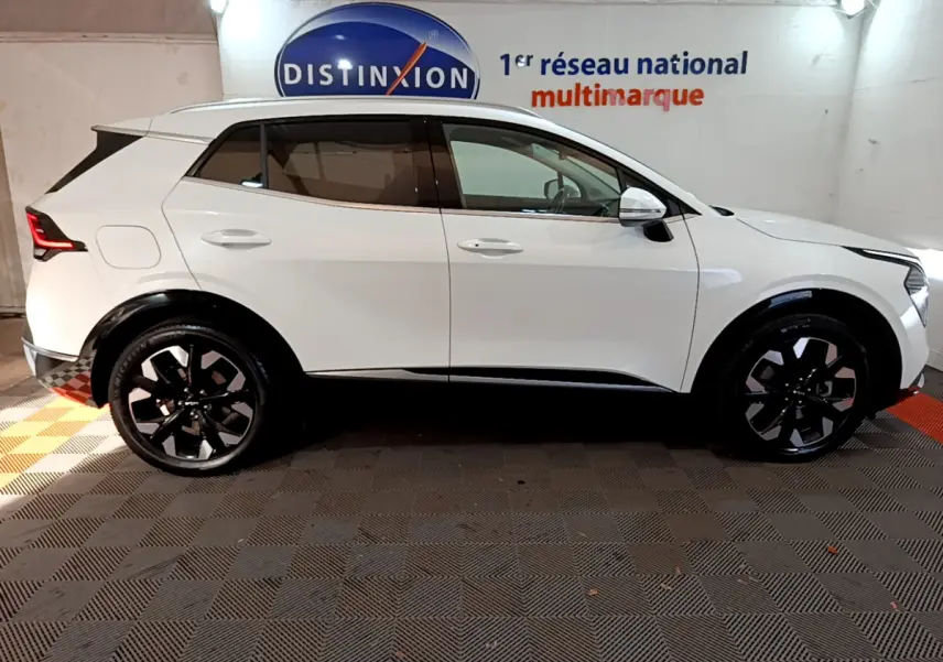 Profil côté gauche du KIA SPORTAGE blanc 2022 avec jantes noires et détails noirs sur les passages de roue.