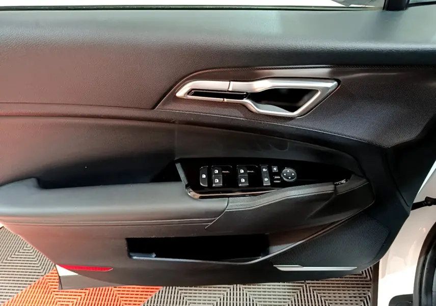 Intérieur côté conducteur de la porte d’un KIA SPORTAGE blanc 2022, avec commandes électriques et poignée argentée.