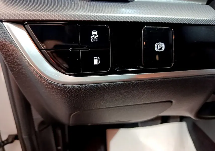 Gros plan sur les commandes noires du tableau de bord du Kia Sportage blanc 2022, avec bouton frein électrique et contrôle traction.