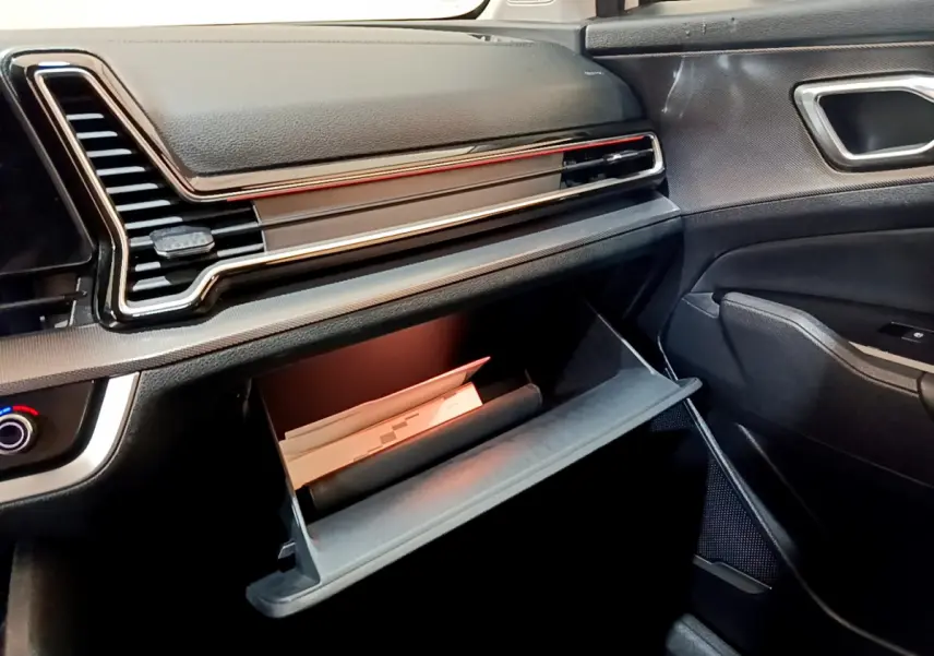 Intérieur du Kia Sportage 2022 hybride rechargeable, vue côté passager sur la boîte à gants ouverte et tableau de bord noir.