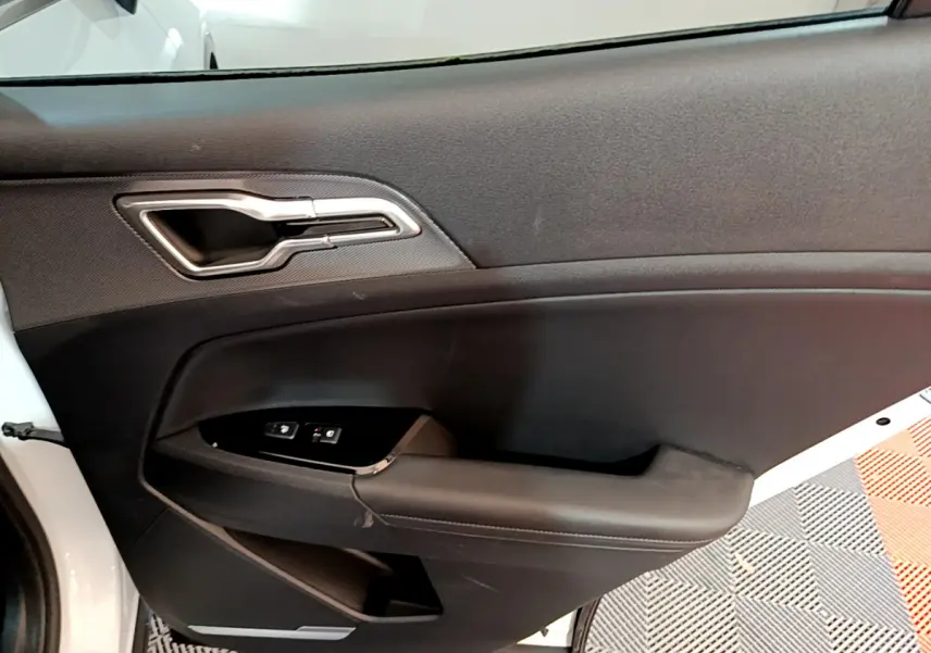 Vue intérieure de la porte côté conducteur du KIA SPORTAGE blanc 2022 avec poignée argentée et commandes vitres.