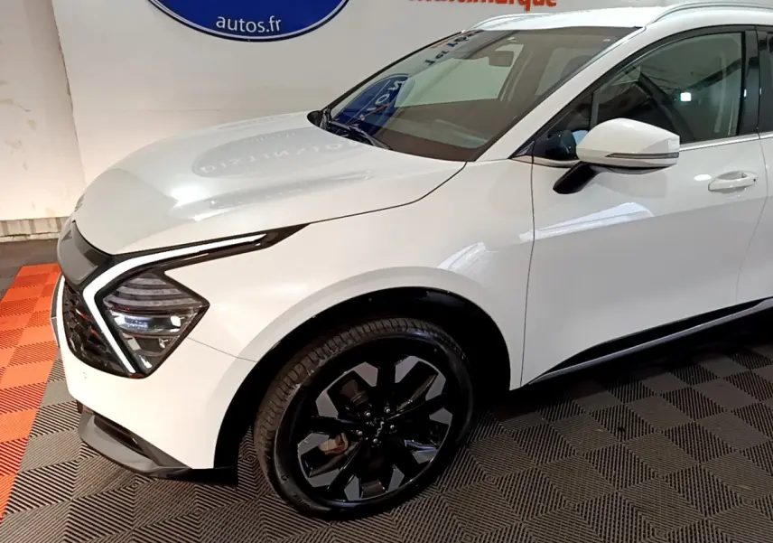 Vue 3/4 avant droit du KIA SPORTAGE blanc avec jantes noires et feux avant LED distinctifs.
