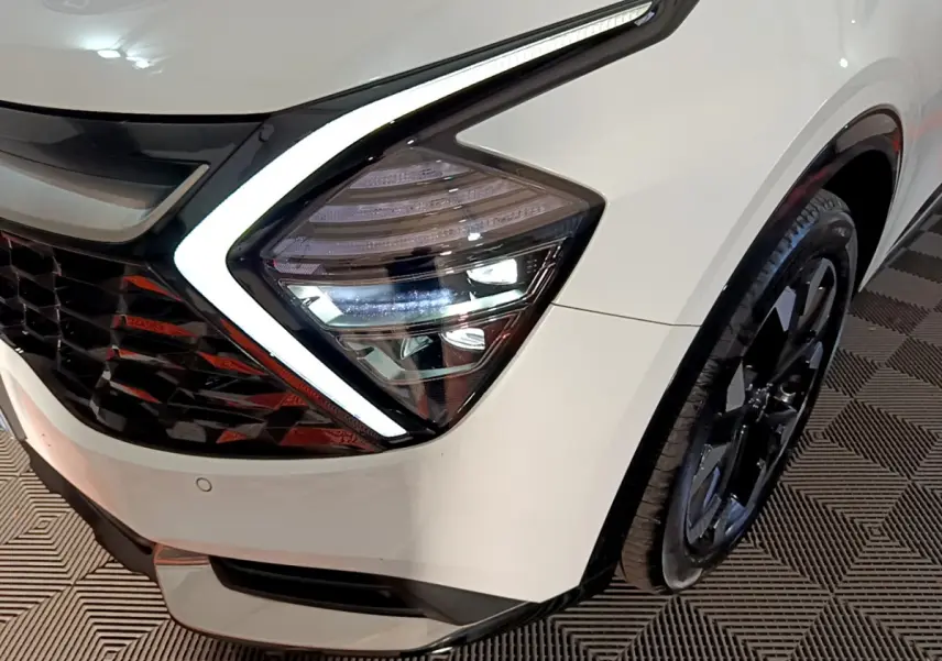 Gros plan sur le phare avant droit blanc du KIA SPORTAGE 2022 avec éclairage LED et jante noire visible.