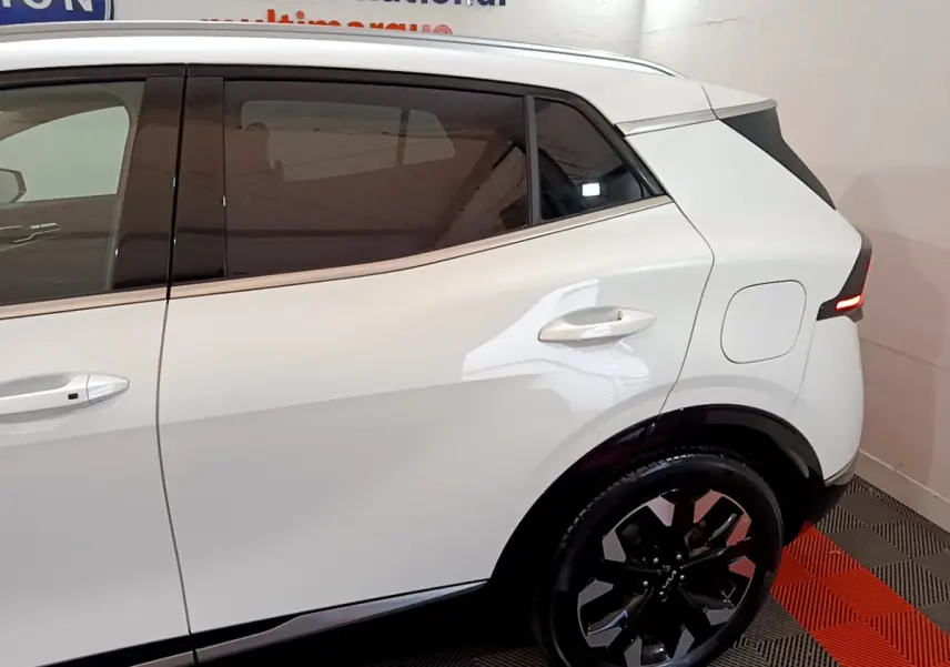 Vue latérale droite du KIA SPORTAGE blanc 2022 avec jantes noires et feux arrière LED allumés.