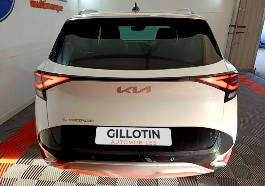 Vue arrière d'un KIA SPORTAGE blanc 2022 avec feux LED allumés et logo KIA visible sur le hayon noir.