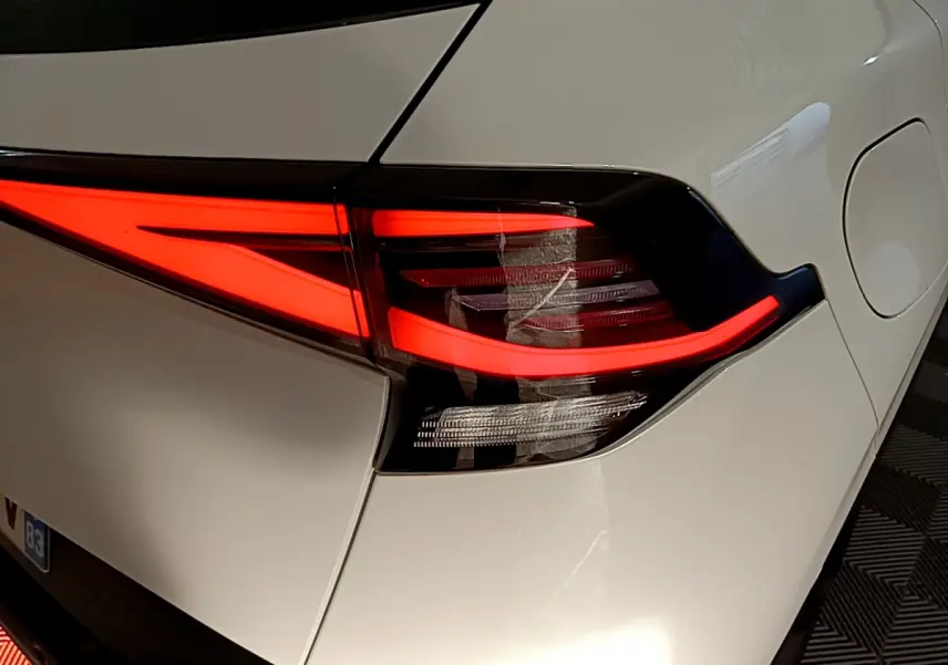 Gros plan sur le feu arrière droit rouge vif du KIA SPORTAGE blanc hybride rechargeable, vue arrière latérale.