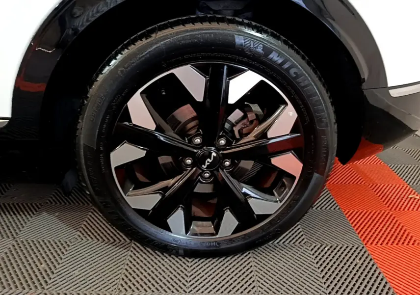 Gros plan sur la roue avant gauche du Kia Sportage blanc 2022, mettant en valeur la jante noire brillante au design moderne.