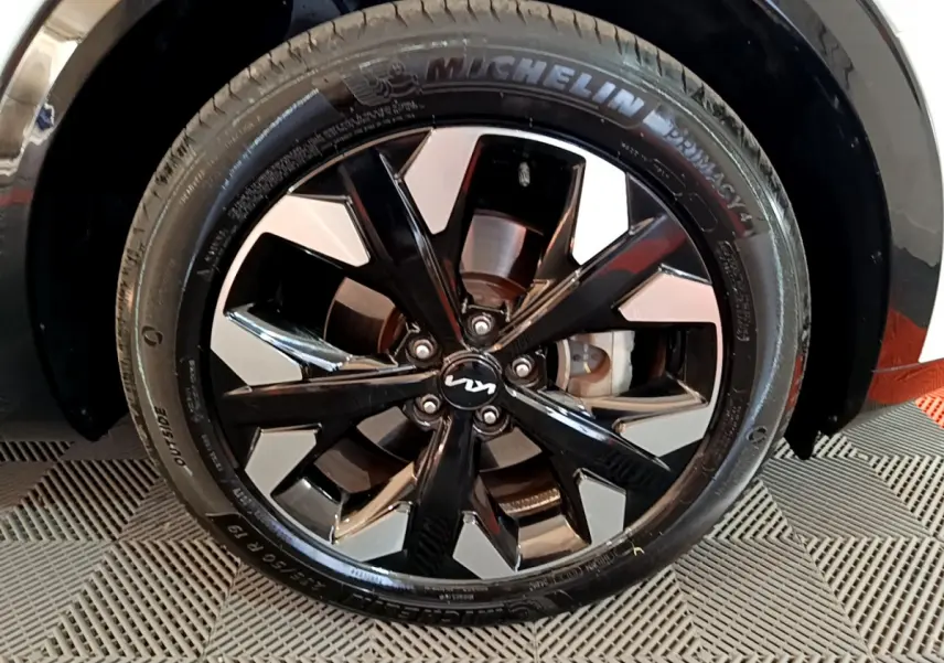 Gros plan sur la roue avant droite du KIA SPORTAGE blanc avec jante alliage noir et argentée au design moderne.